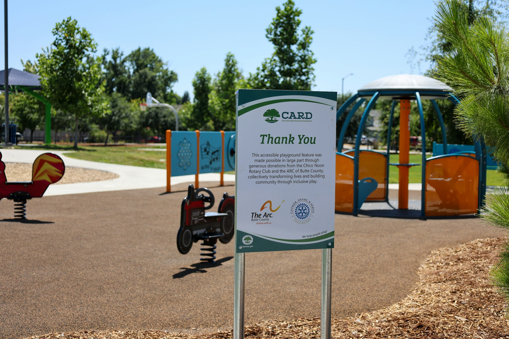 The image shows a playground sign thanking donors for creating an accessible play area to build community through inclusive play.