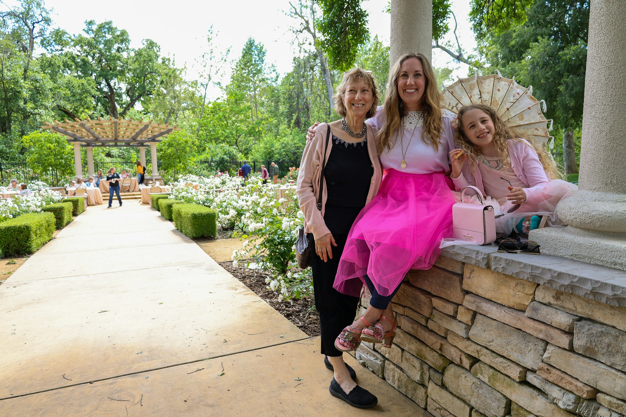 May contain: path, walkway, clothing, dress, flagstone, formal wear, accessories, bag, handbag, evening dress, footwear, shoe, jewelry, necklace, garden, nature, outdoors, arbour, person, sandal, coat, and glasses
