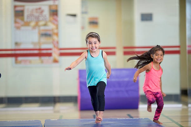 Two girls running and smiling in a gym.