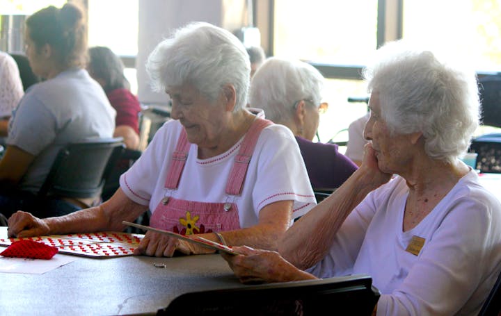 Elderly women sitting at a table, playing a game with red markers.