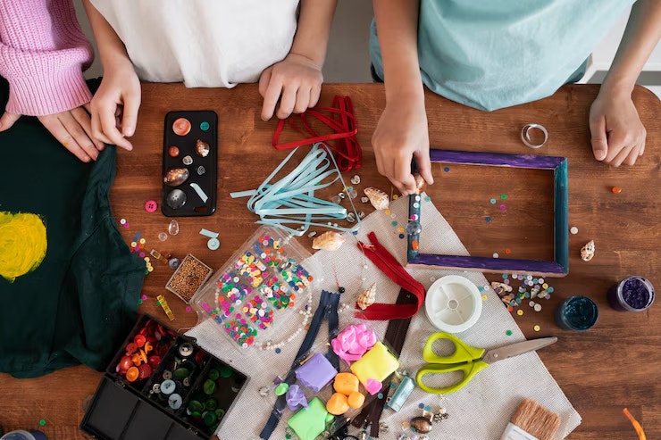 Art and craft materials on a table with three children preparing to make creative projects.