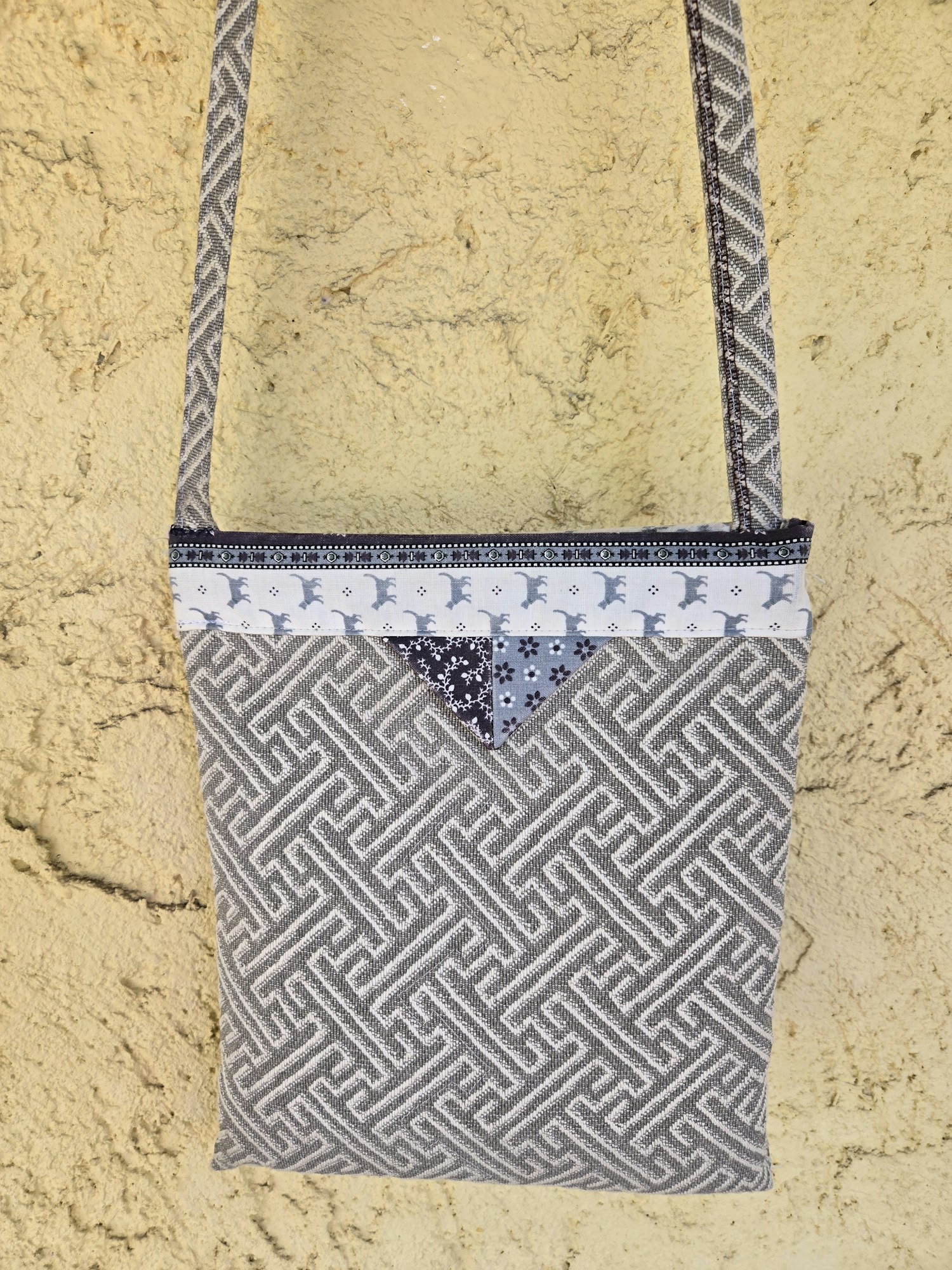 A patterned handbag featuring a mix of geometric designs and solid fabric, set against a textured yellow background.