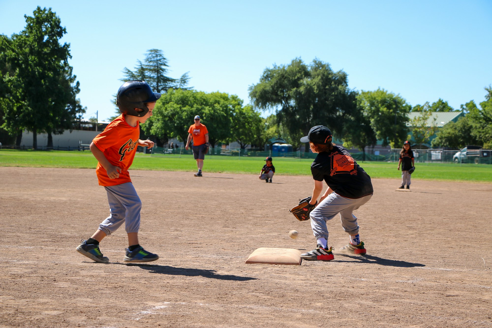 Kids playing baseball, one running to a base and another trying to catch the ball.