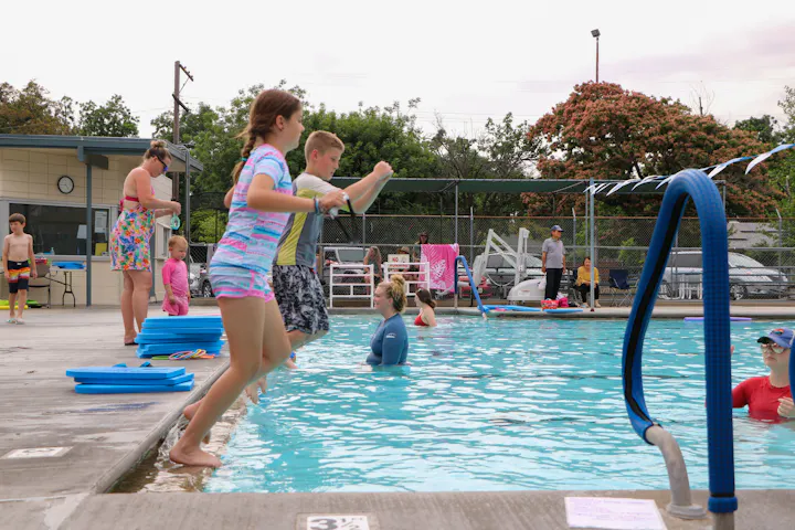 Children playing and jumping into a swimming pool with adults supervising nearby.