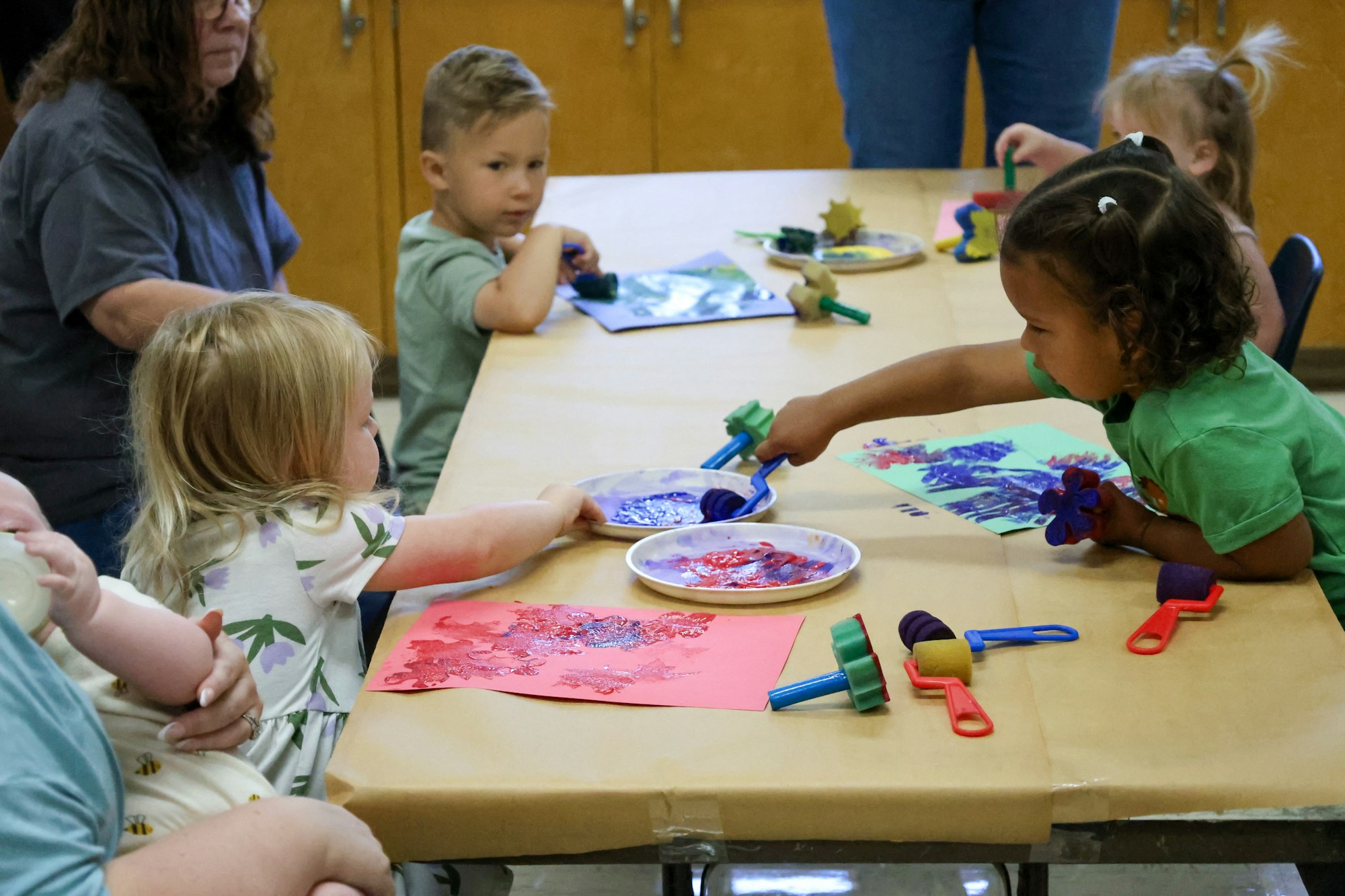 Children engaged in a colorful painting activity with sponges and paint rollers on paper.