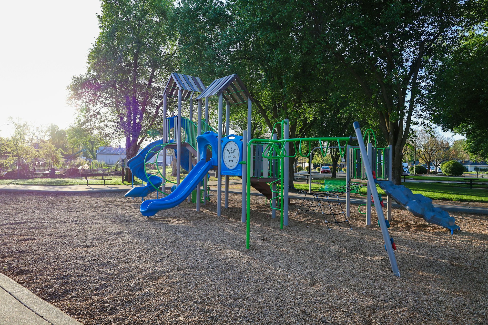 A playground with slides, climbing structures, and a swing set in a park with trees.