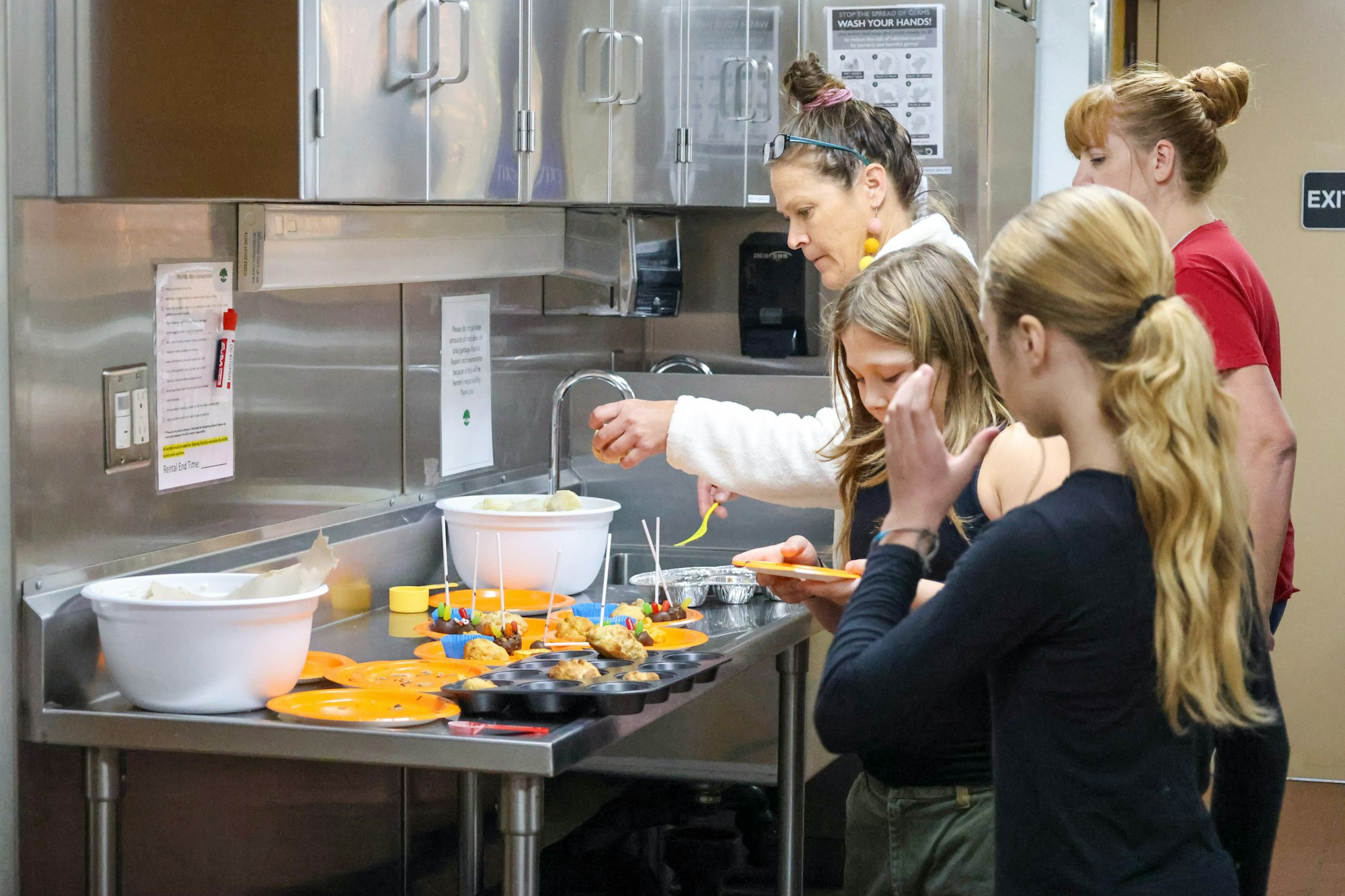 People preparing food in a kitchen with trays and bowls on a countertop.