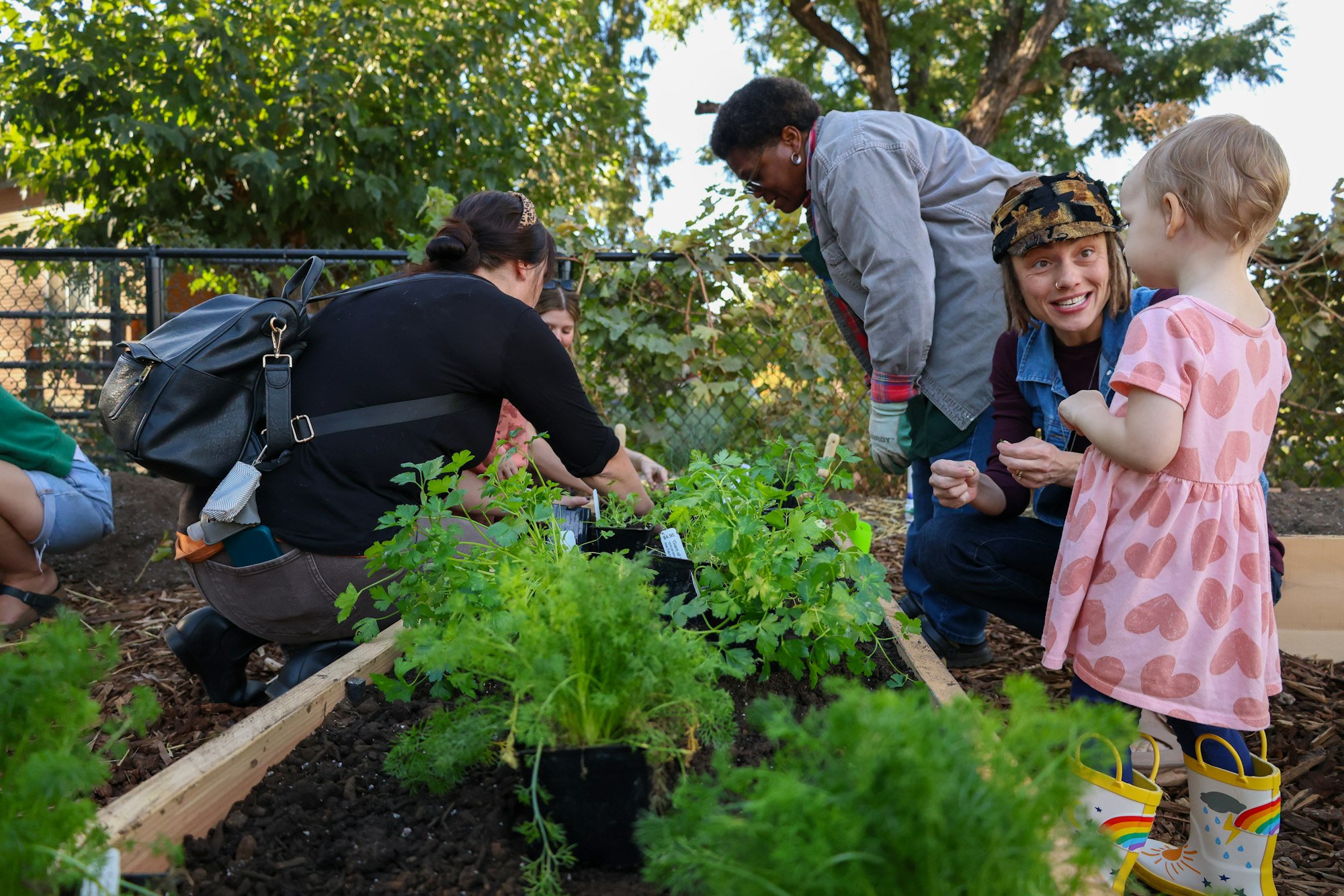 People gardening together; a child observes, surrounded by plants and greenery.