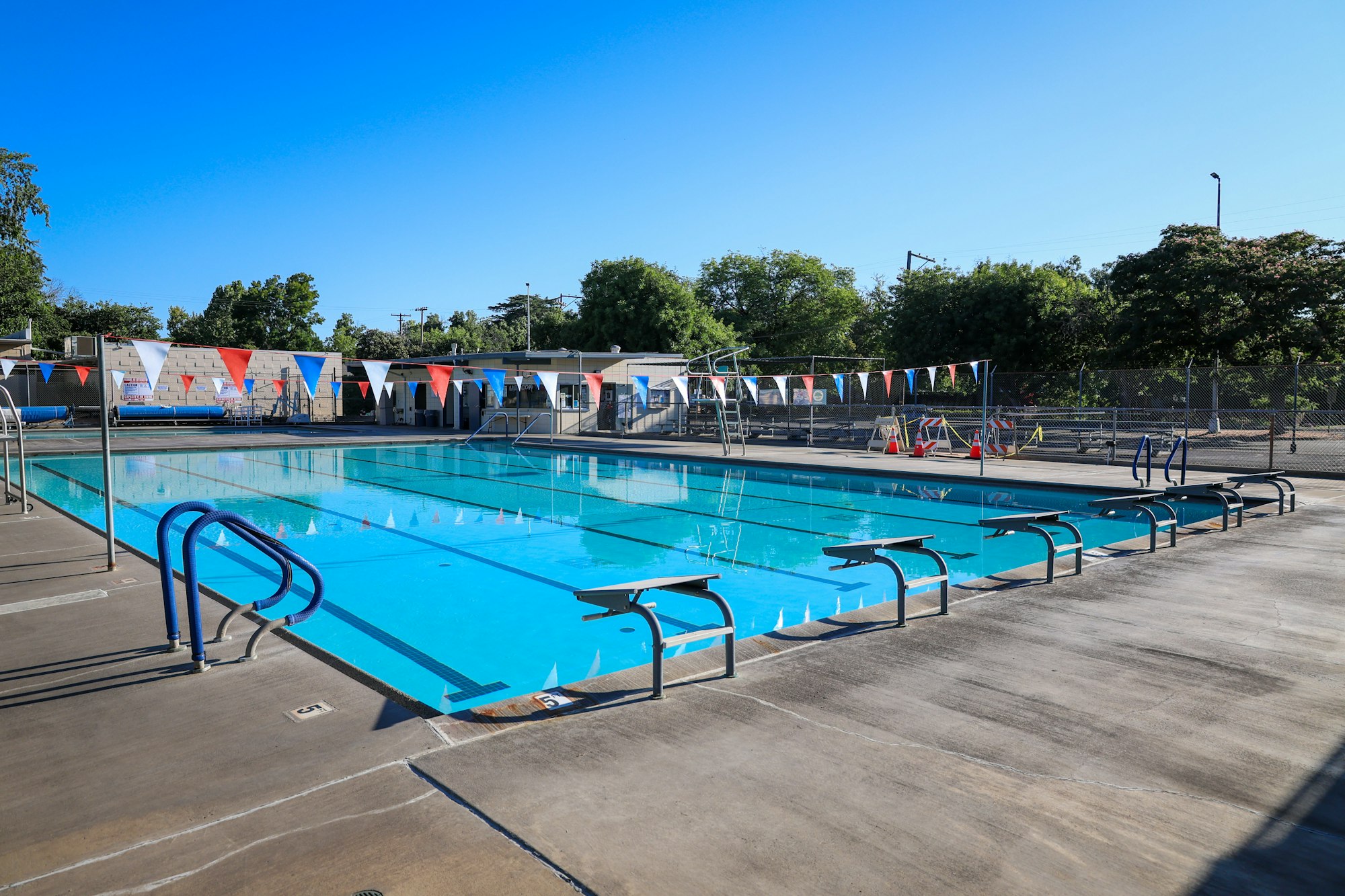 An empty outdoor swimming pool with diving boards and colorful flags on a sunny day.