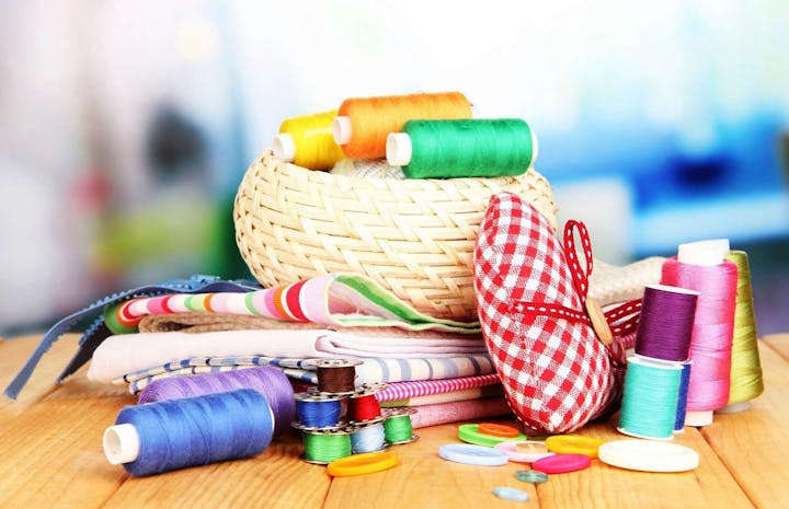 Colorful sewing supplies: threads, fabric, a pincushion, buttons, and a straw basket on a wooden table.