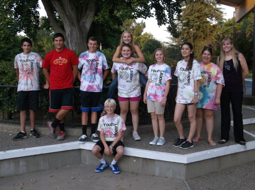 A group of people posing outside, some wearing tie-dye shirts that say "Youth Leader 2013."
