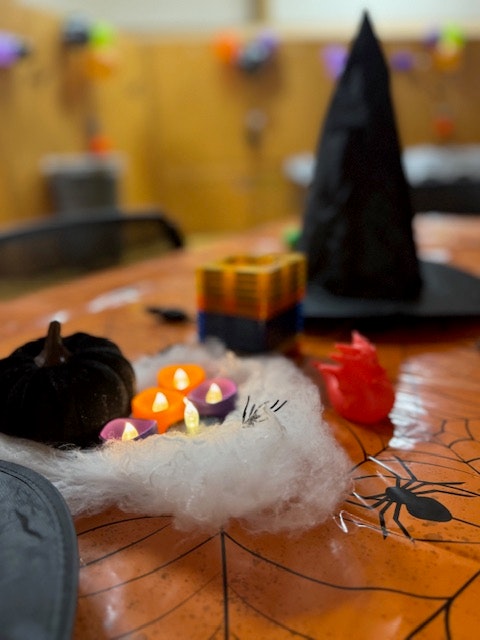 A Halloween-themed table with decorations including a witch hat, candles, a black pumpkin, and cobwebs.