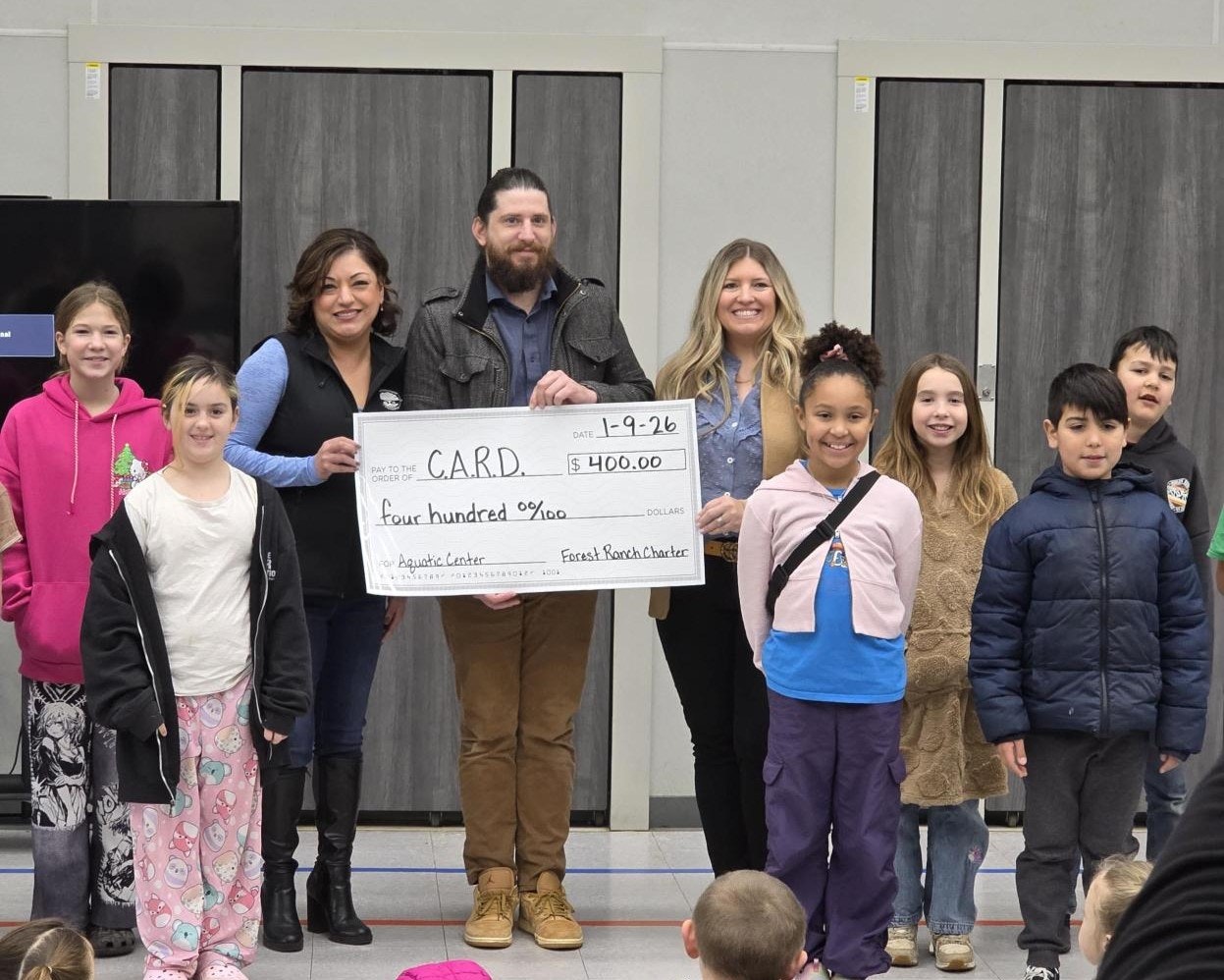 A group of adults and children celebrate a $400 check presentation for the Aquatic Center at Forest Ranch Charter.