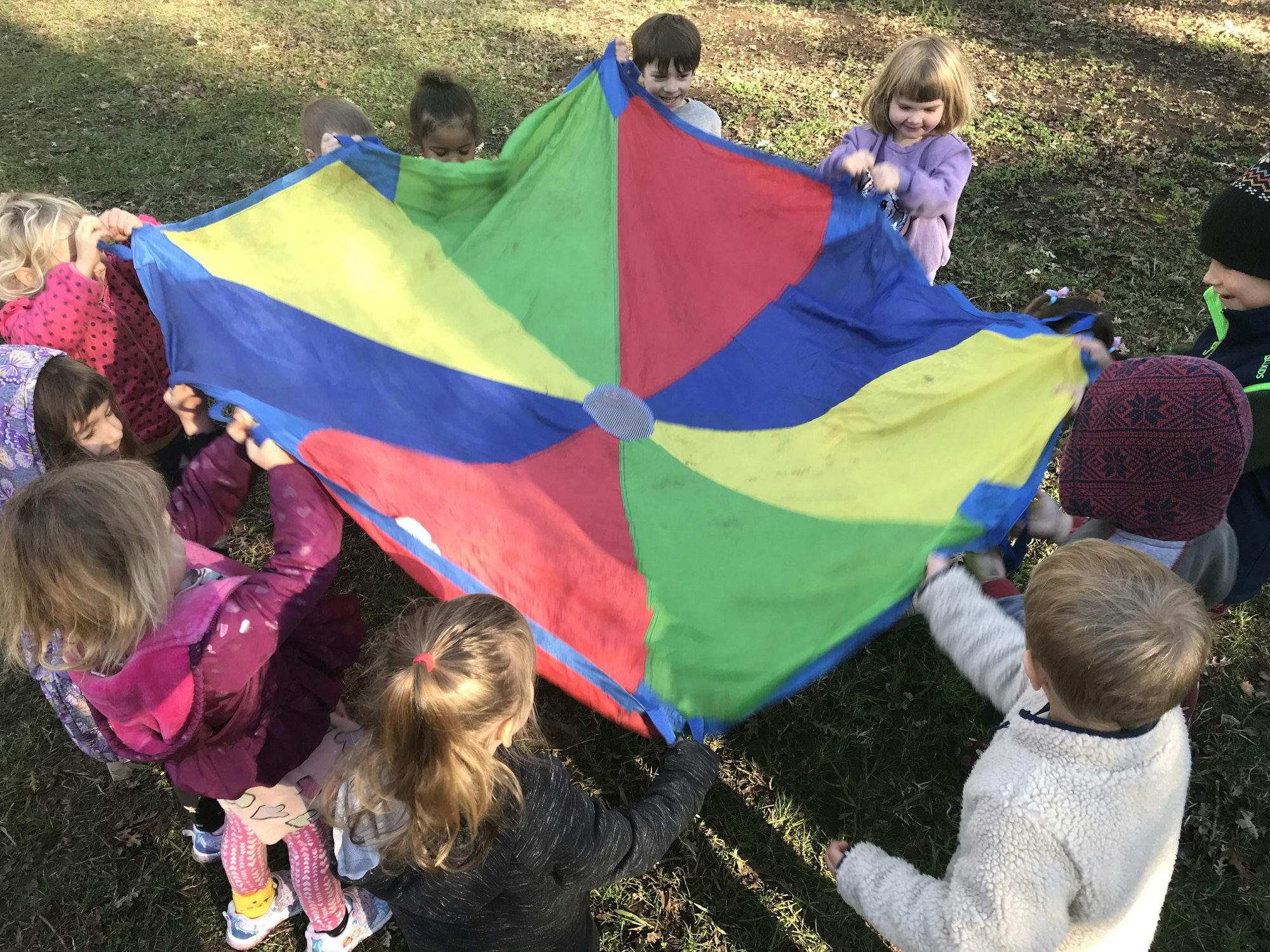 Children holding a colorful parachute outdoors.