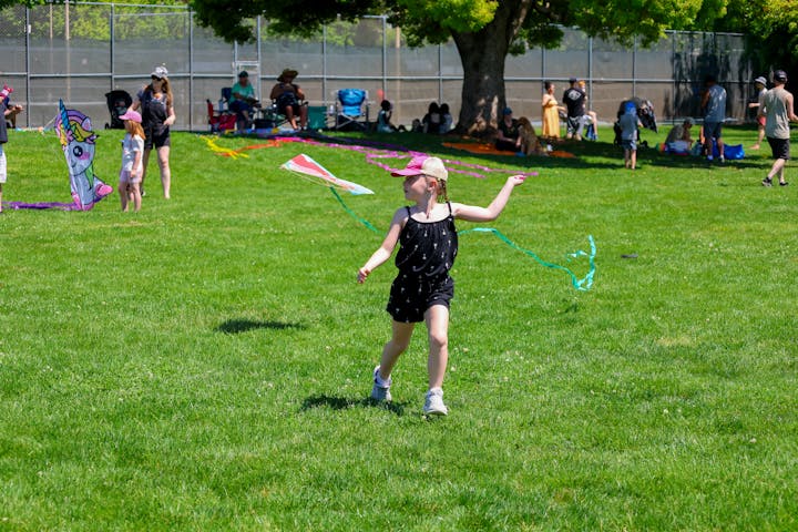 A child flying a kite in a park with people in the background.