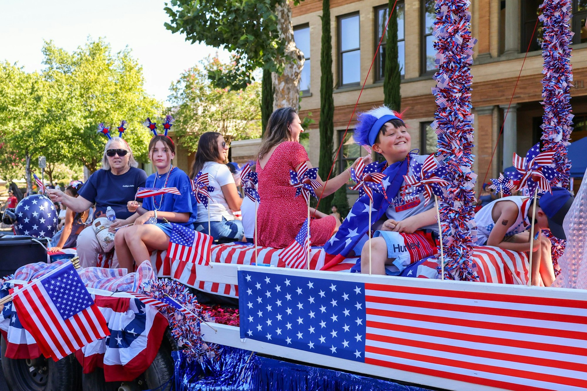 A festive parade float decorated in red, white, and blue, with people celebrating, holding flags and wearing themed attire.