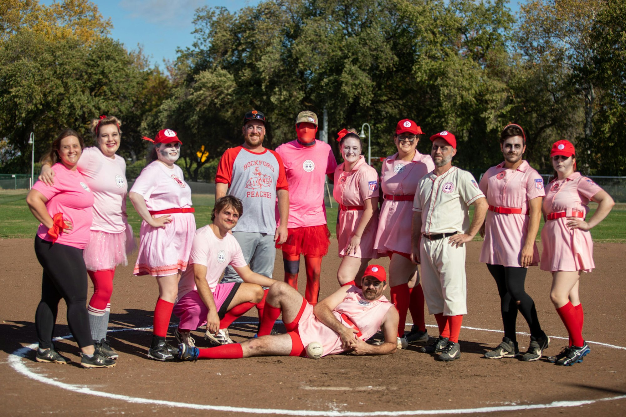 A group of people in costumes and pink team uniforms posing on a baseball field.
