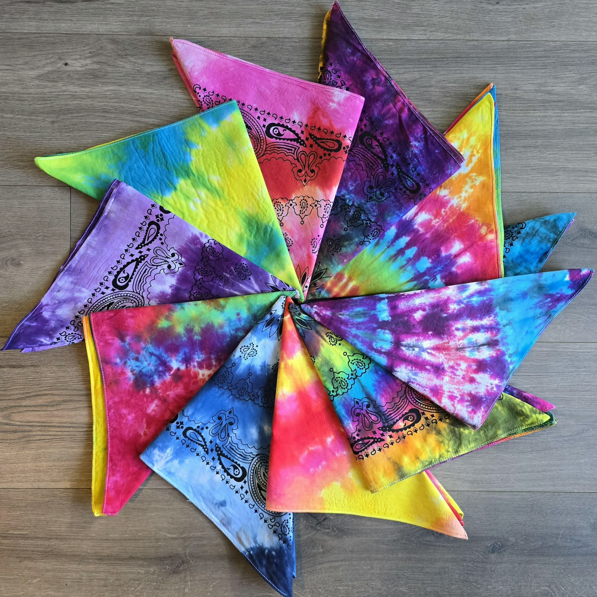 Colorful tie-dye bandanas arranged in a circular pattern on a wooden surface.