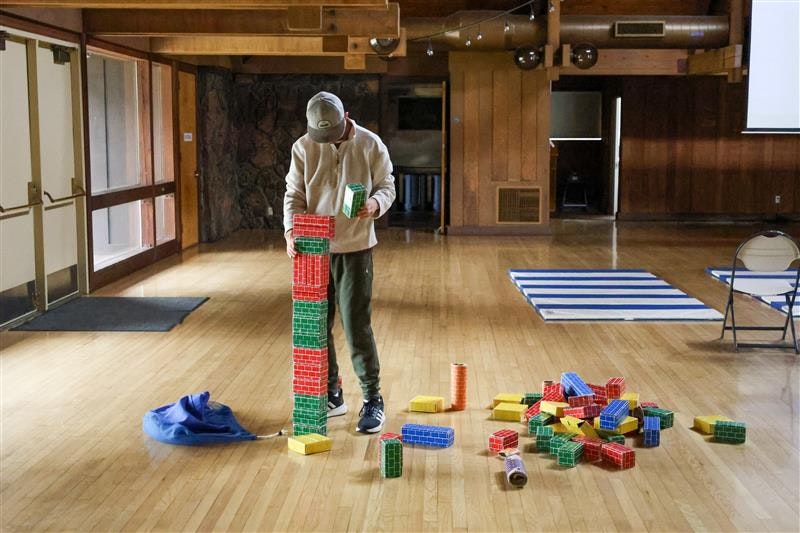 A person stacking colorful plastic blocks in a spacious room with wooden floors.