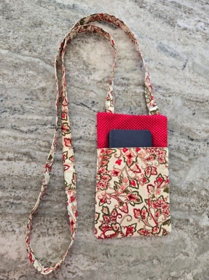 Floral fabric pouch with a long strap, containing a phone inside a pink lining.