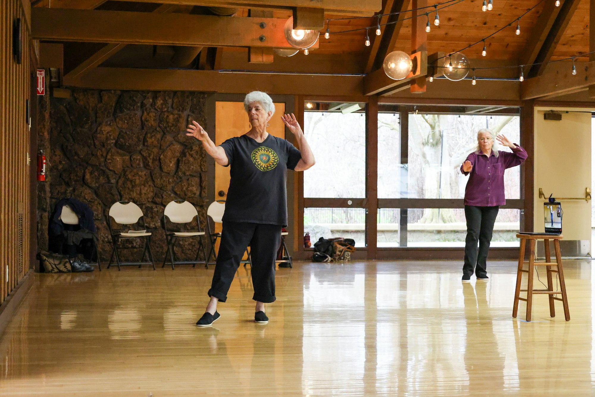 Two people practicing Tai Chi in a spacious room with large windows and wooden floors.