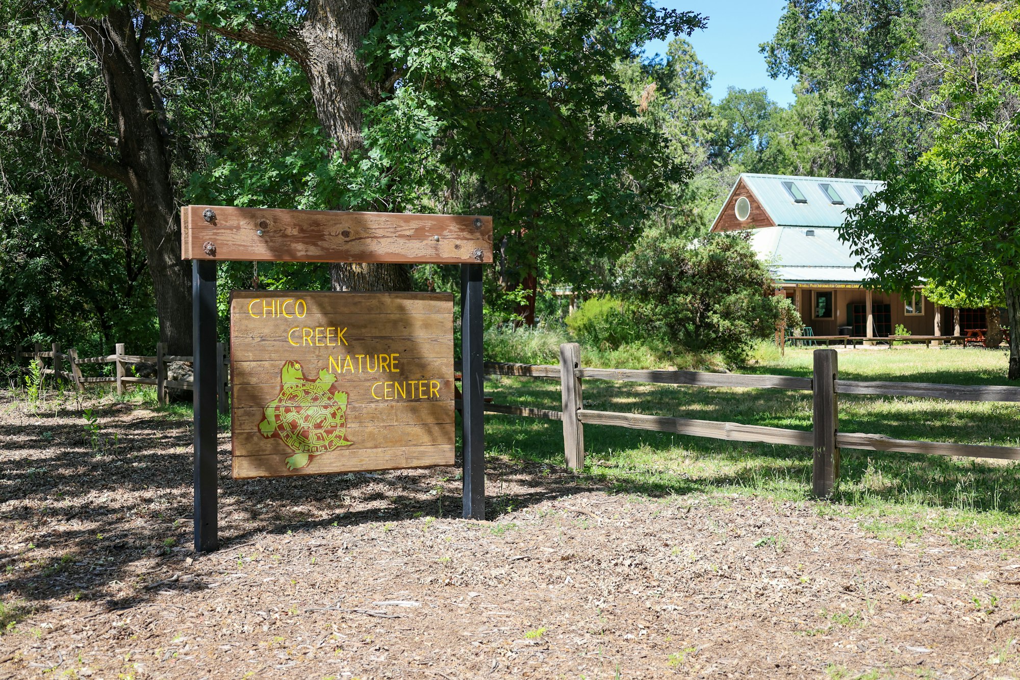 Sign reading "Chico Creek Nature Center" in a wooded area with a building in the background.