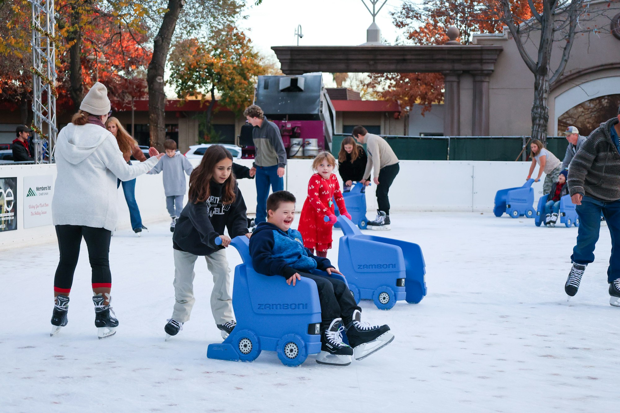 People ice skating on a rink, using blue skating aids shaped like mini Zambonis.