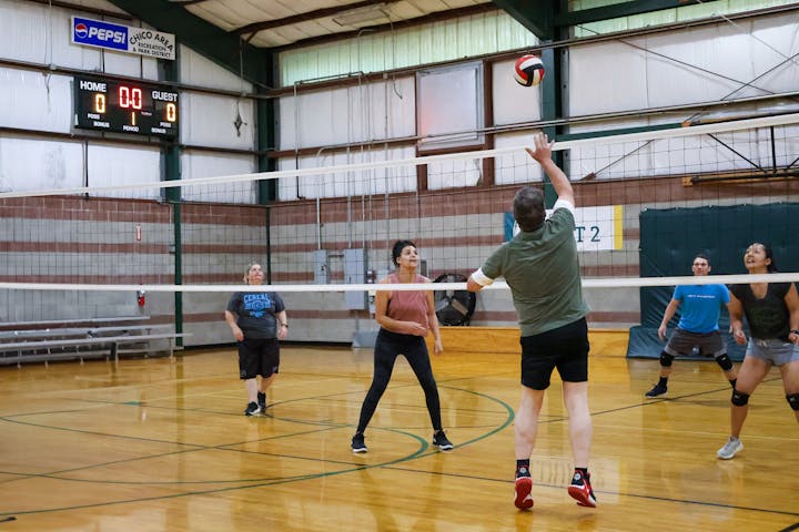 People playing volleyball indoors with a scoreboard in the background.