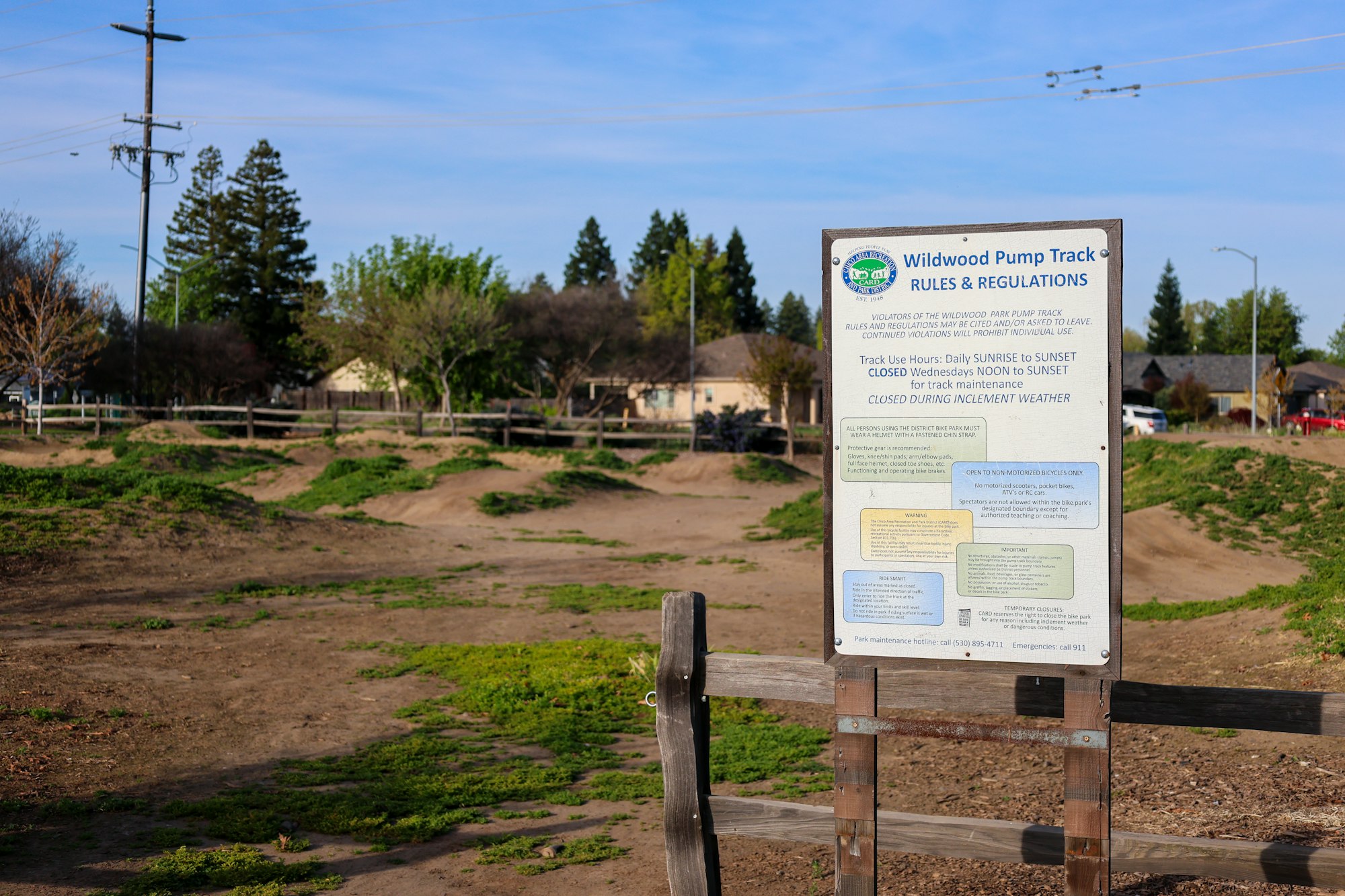 A sign for Wildwood Pump Track with rules and a dirt bike track in the background.