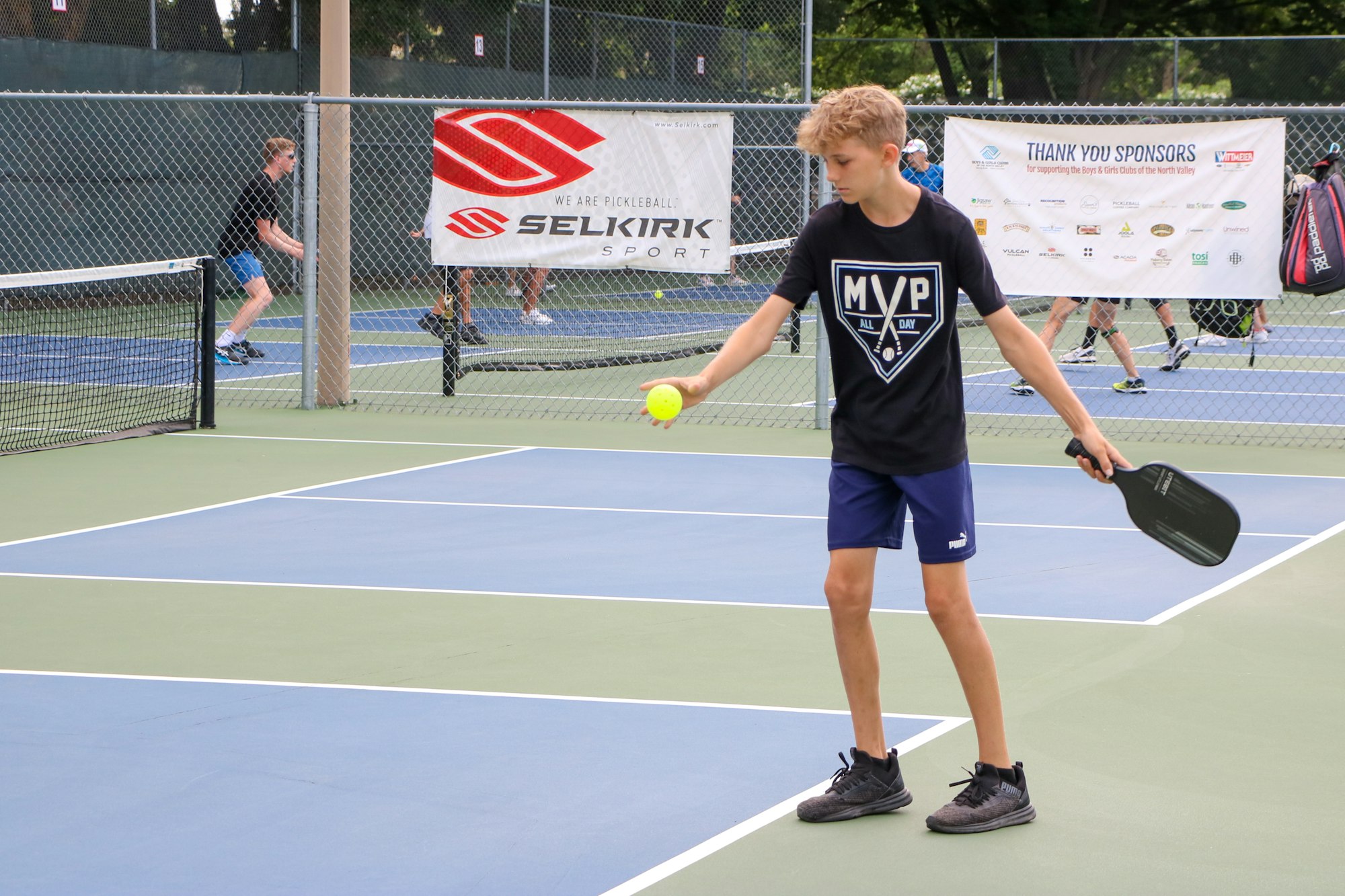 A young person playing pickleball on a court with others in the background.