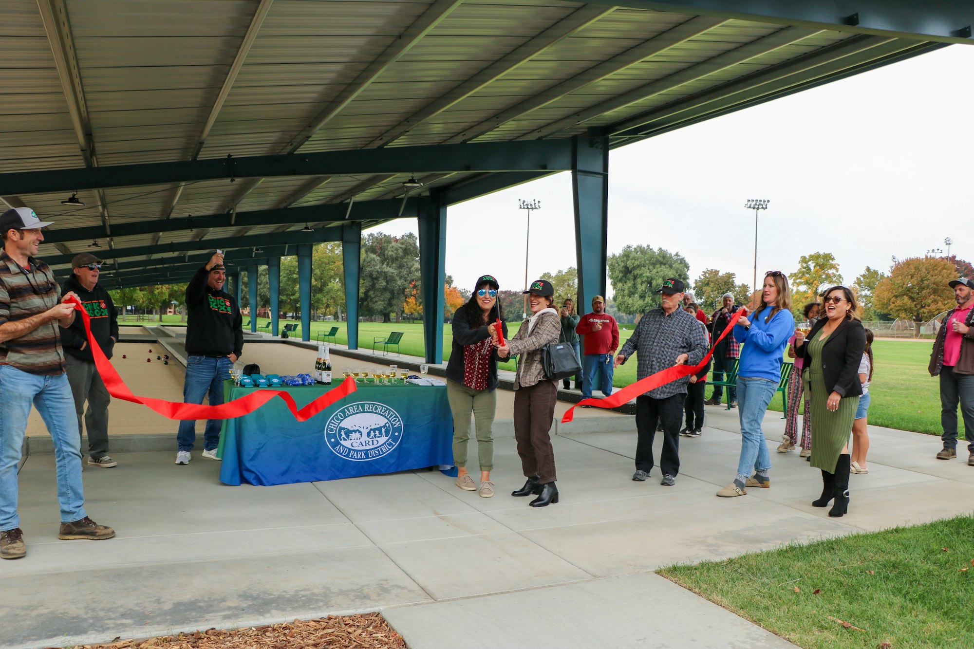 A group of people participating in a ribbon-cutting ceremony outdoors.