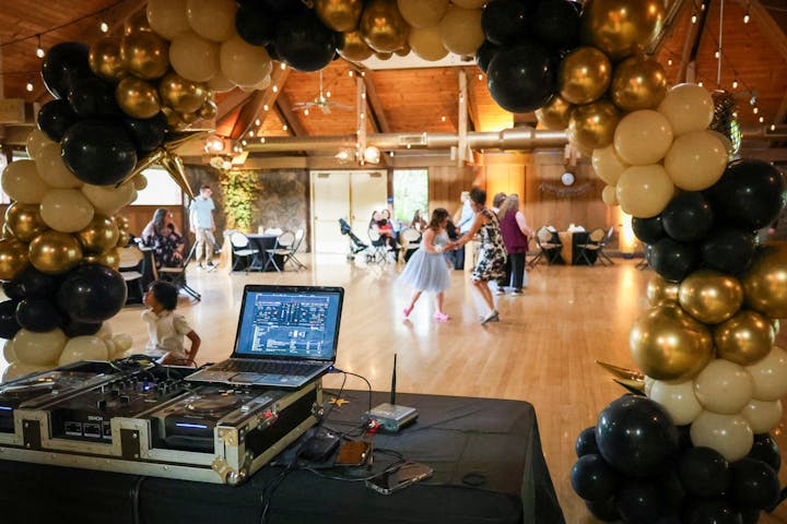 DJ setup at a party with people dancing and balloon decorations.