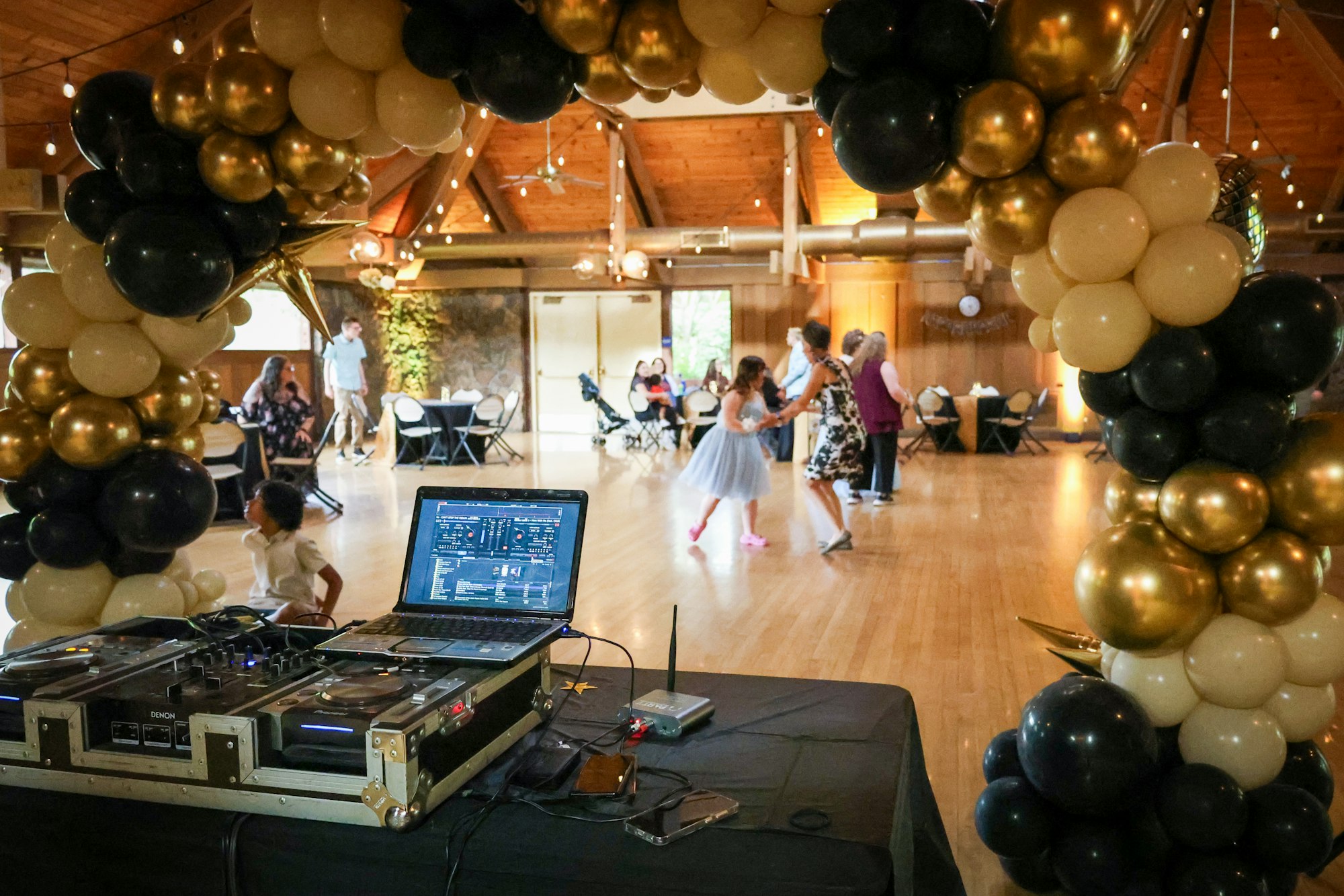 DJ setup at a party with people dancing and balloon decorations.