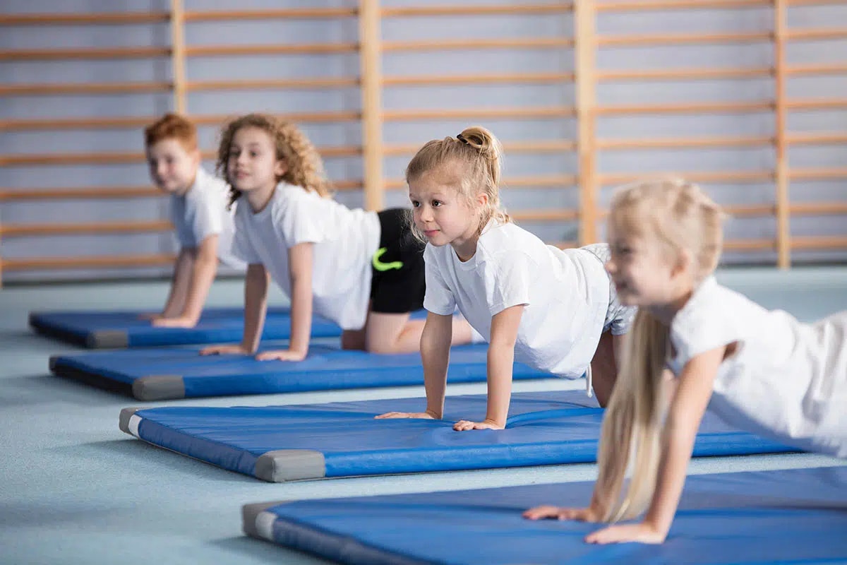 Children doing push-ups on gym mats in a physical education class.