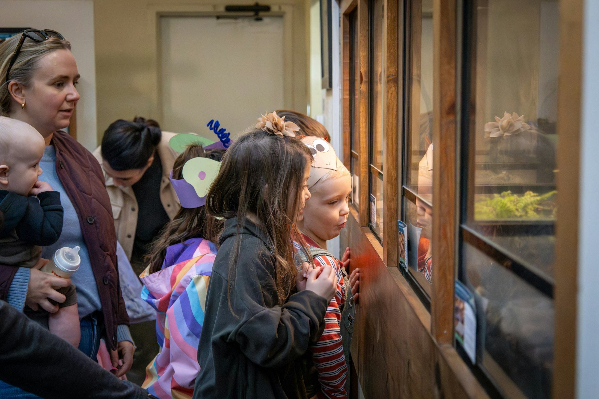 A group of children and adults gather, curiously peering into display cases, likely at a zoo or aquarium.