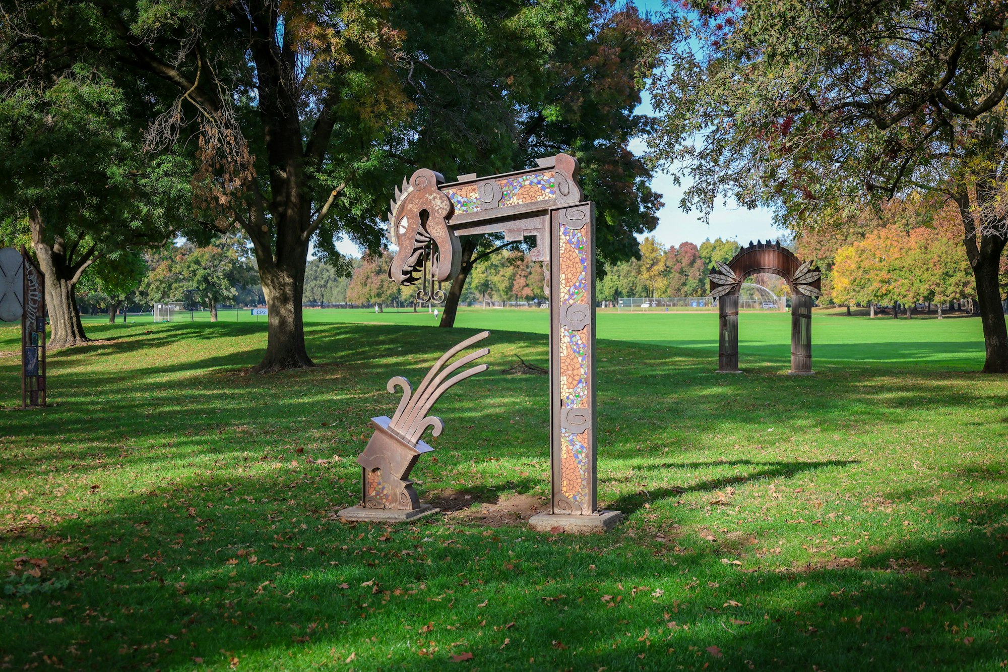 An artistic sculpture in a park with trees and open grassy areas.