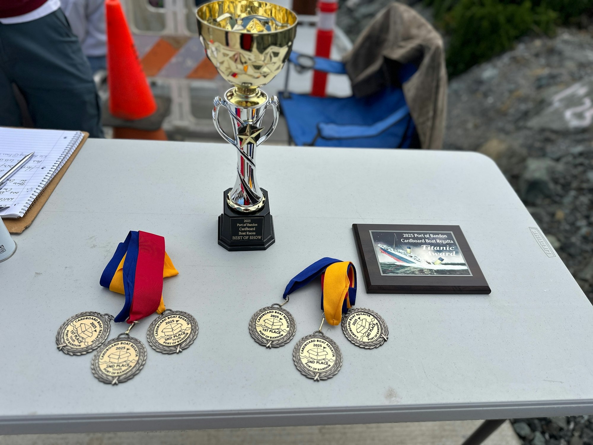 Trophy, medals, and a plaque on a table for the 2023 Port of Bandon Cardboard Boat Regatta.