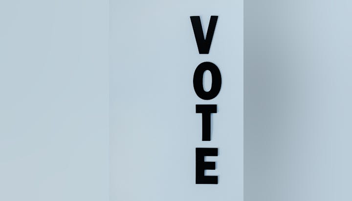 The image shows the word "VOTE" arranged vertically on a light background.