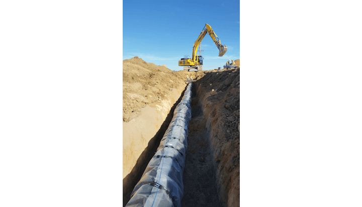 Large pipe in a trench with construction workers and an excavator.