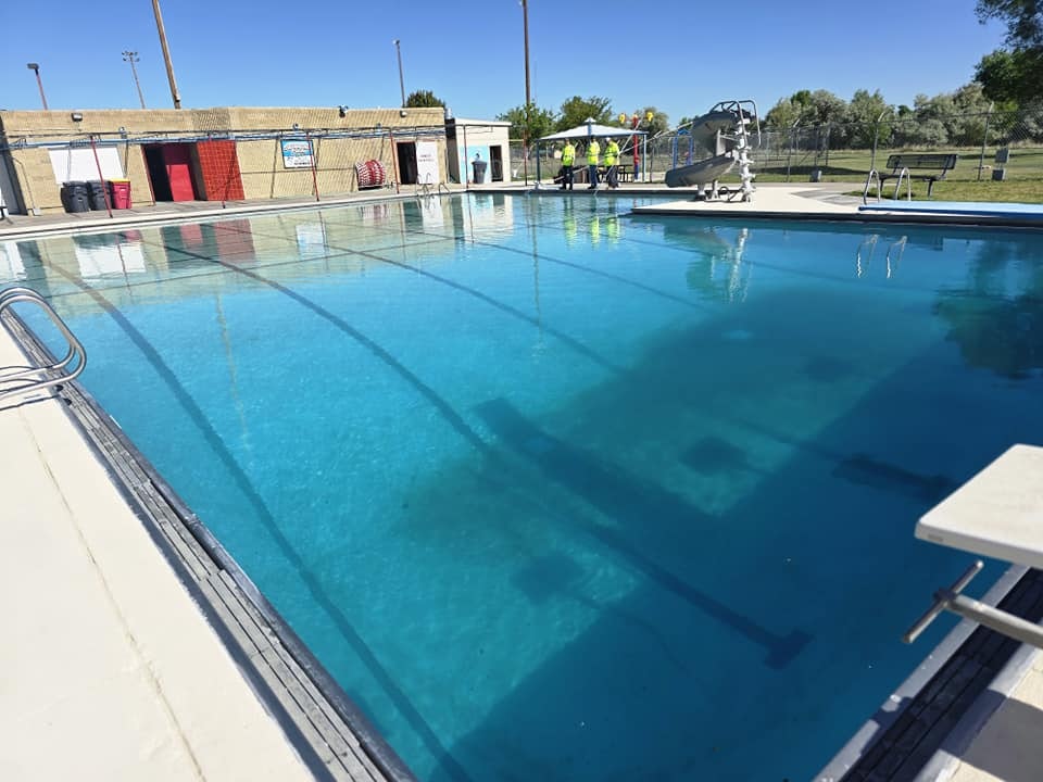 Outdoor swimming pool with clear blue water, diving board, and poolside facilities under a sunny sky.
