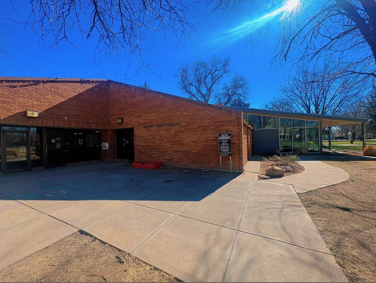 The image shows a building labeled "Rocky Ford Library," featuring a mix of brick and glass architecture under a clear blue sky.