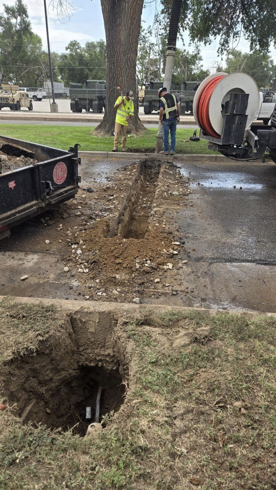 Workers near a trench and equipment, possibly for utility maintenance or installation.