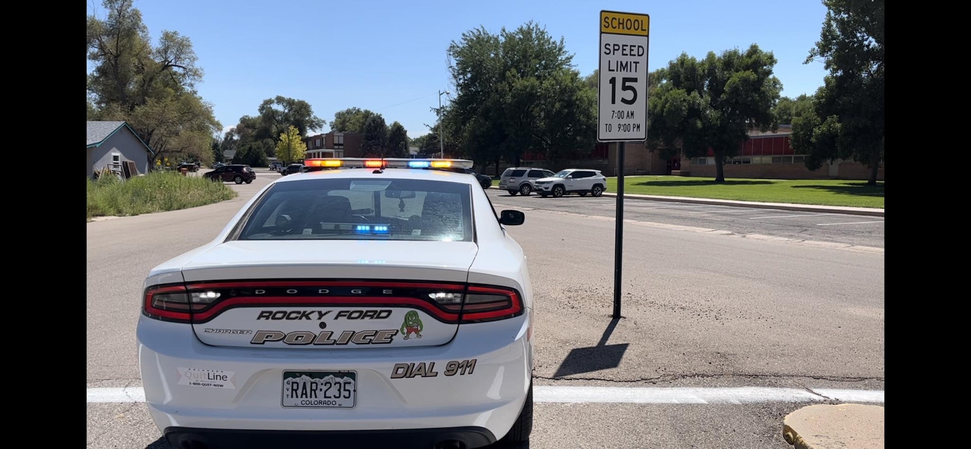 Police car with lights on near school zone speed limit sign (15 mph).