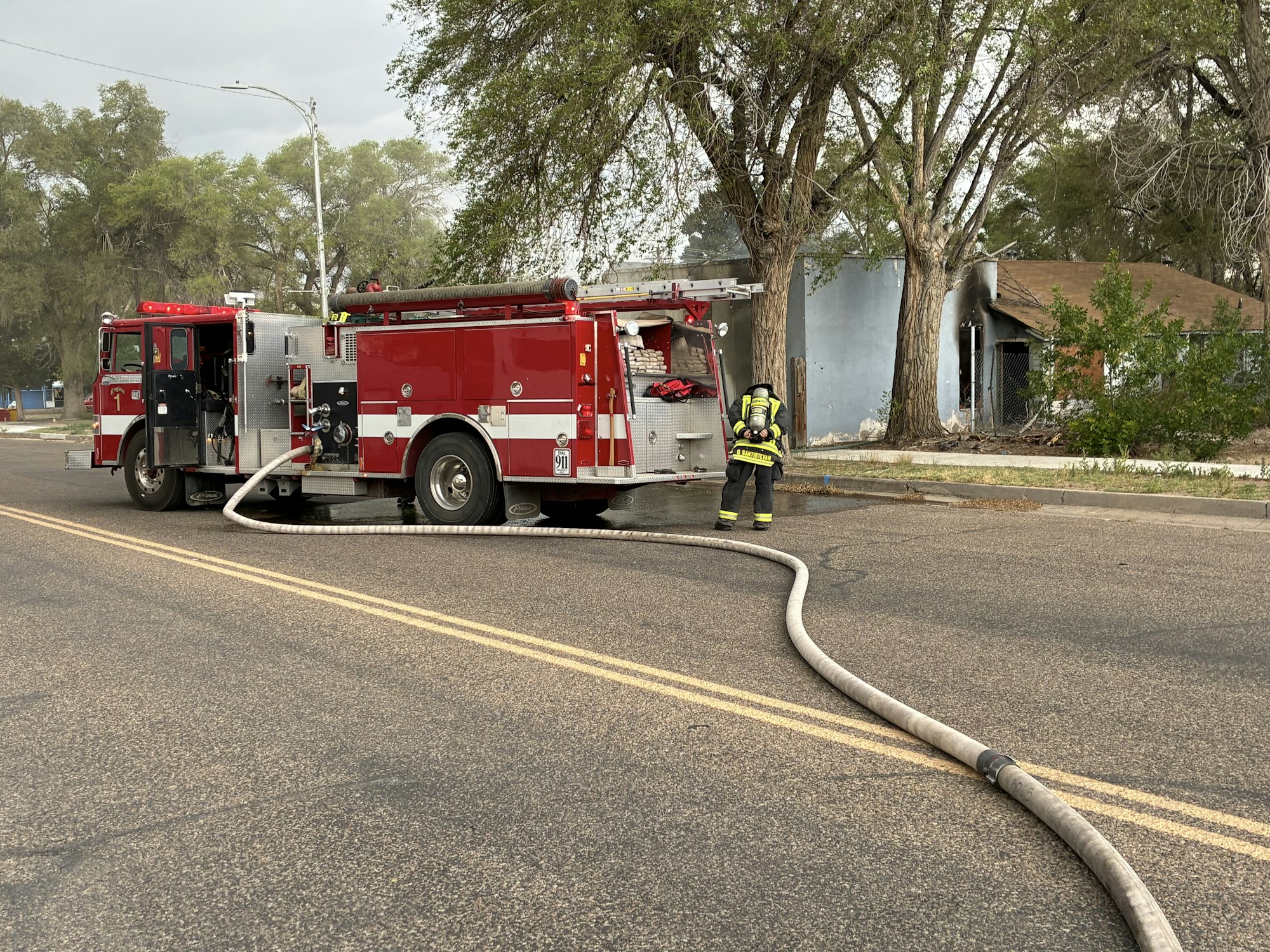 A fire truck is parked on the street, and a firefighter is managing a hose near a damaged building.