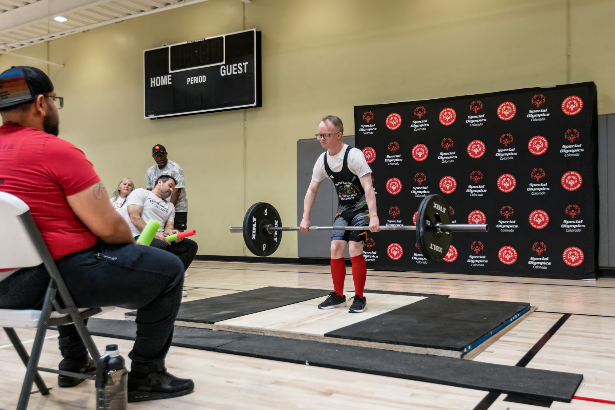 A person is competing in a weightlifting event, with spectators and coaches watching in a sports setting.