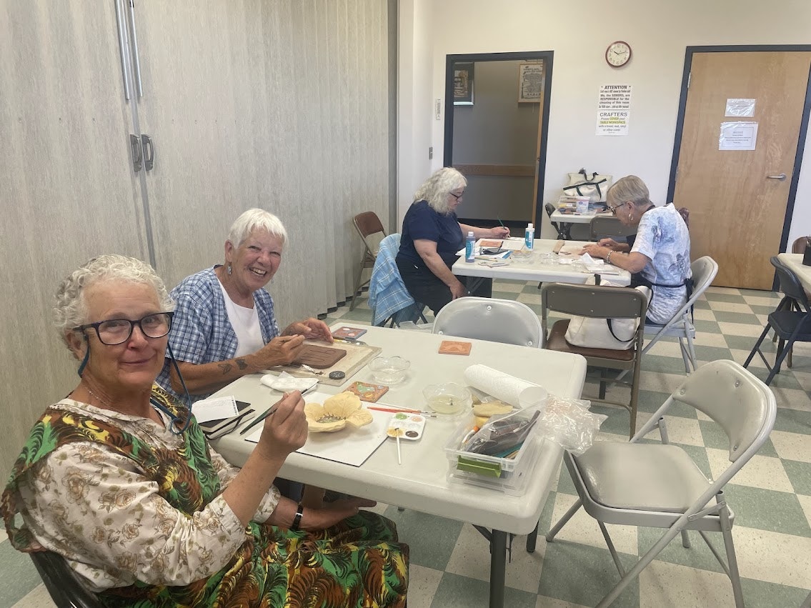 People sitting at tables engaged in crafts and painting, smiling and enjoying their activity.