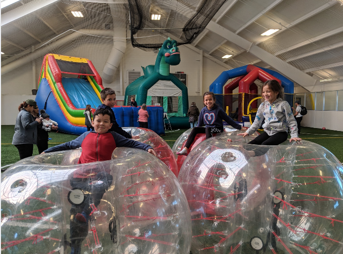 Children playing with inflatable bubbles and bounce houses in an indoor play area.