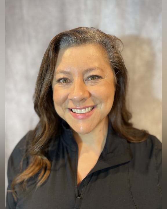 A smiling woman with brown hair in a black shirt against a textured backdrop.