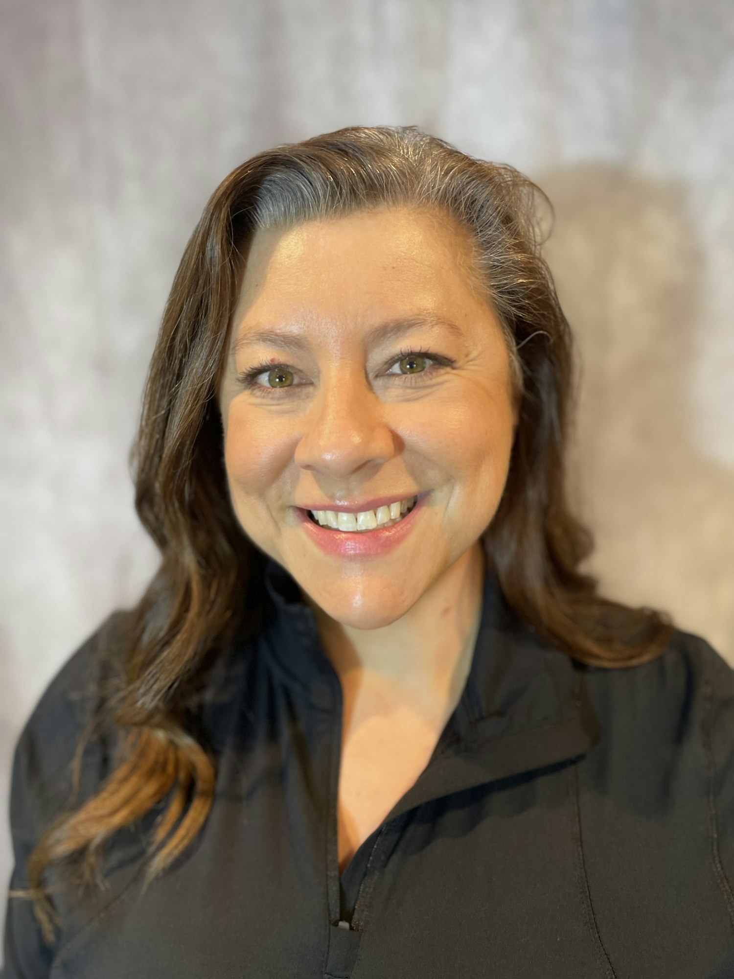 A smiling woman with brown hair in a black shirt against a textured backdrop.