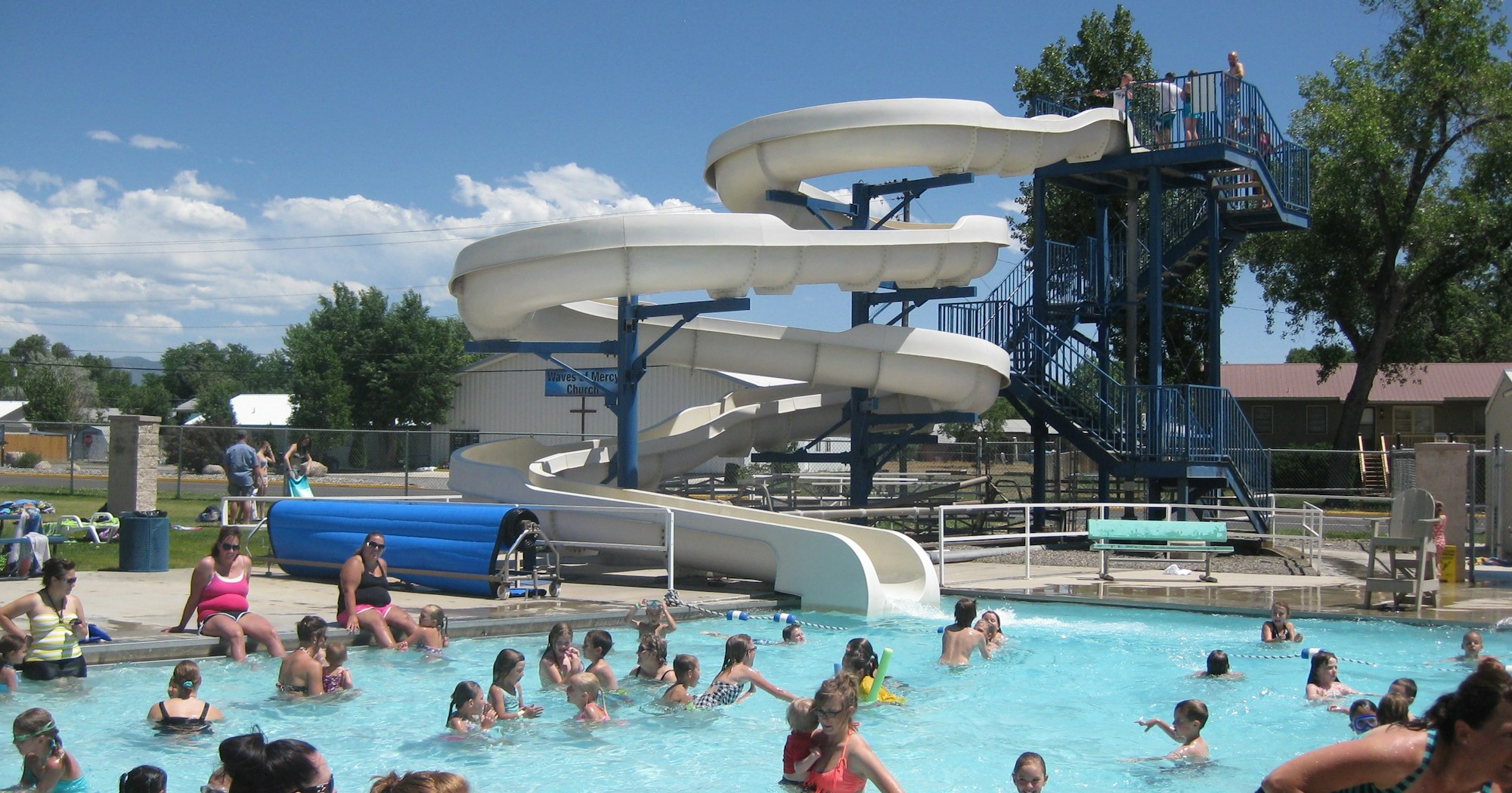 Outdoor swimming pool with people and a water slide.